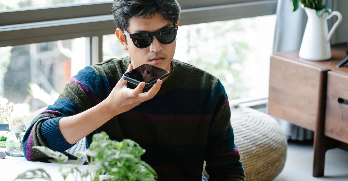 A man uses his smartphone's voice assistant, holding the phone up to speak a question.