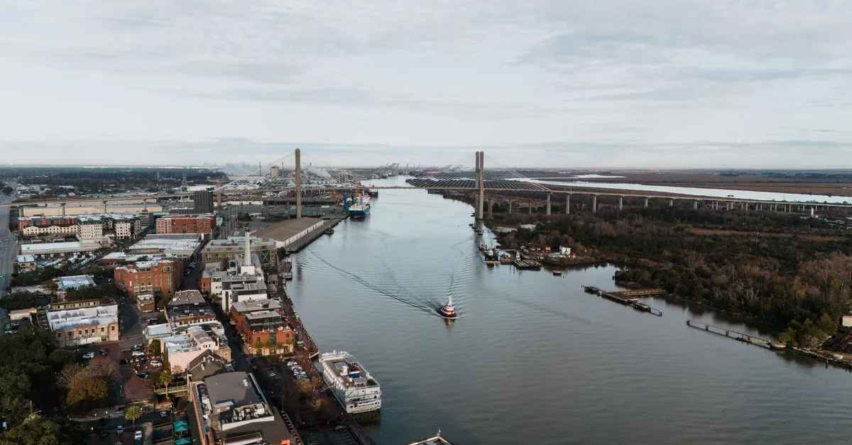 Aerial view of the Savannah River with the Talmadge Memorial Bridge, the River Street waterfront, and port cranes in the distance, Savannah, Georgia.