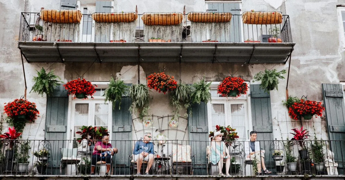 People relaxing on a flower-covered cast-iron balcony in the New Orleans French Quarter, the neighborhood culture local SEO is built around.