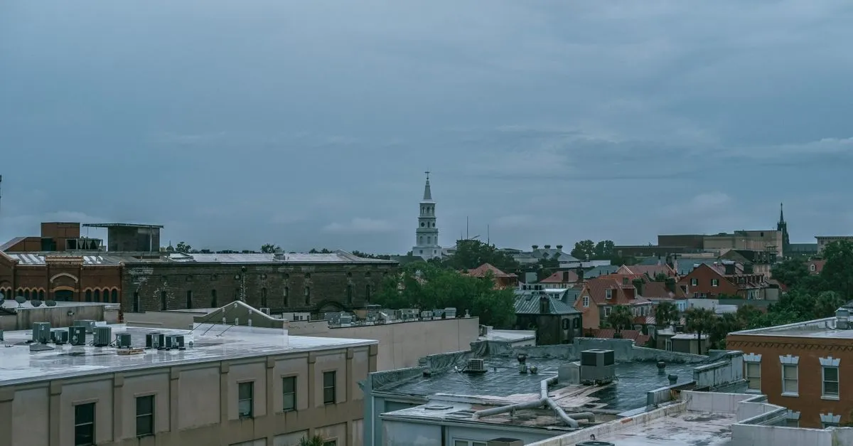 Aerial view of downtown Charleston, South Carolina rooftops with a historic white church steeple rising above under an overcast sky.
