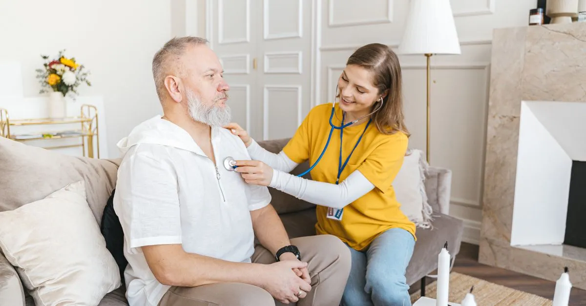 A visiting home health nurse checks an older patient with a stethoscope during a skilled in-home nursing visit.