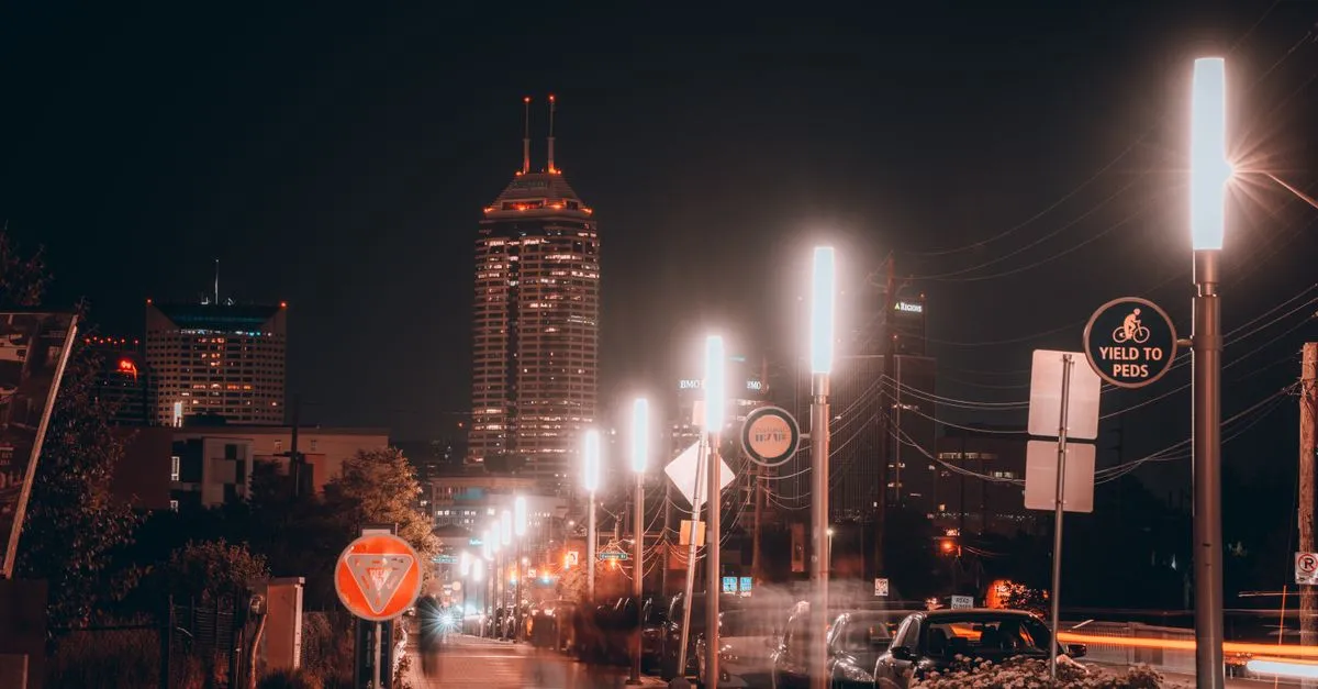 The Indianapolis skyline glowing at night behind an illuminated downtown pathway near the canal.