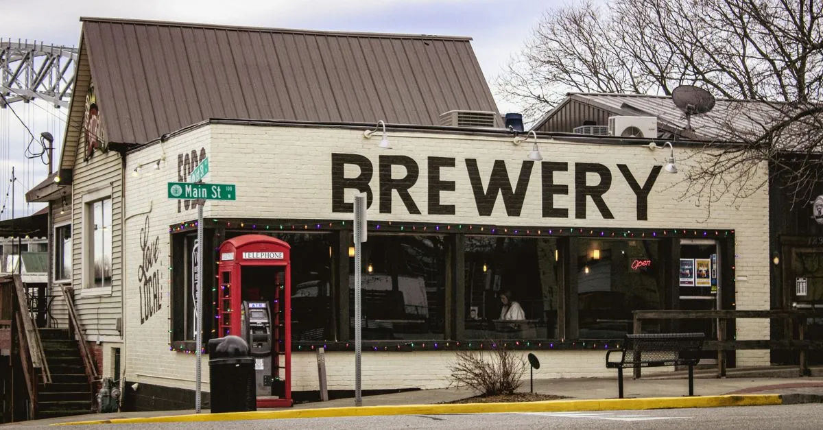 A quiet small-town American main street with a brewery and storefronts under an overcast sky and bare trees.