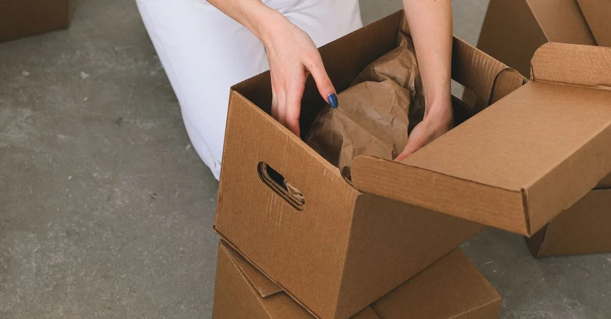 Person packing household belongings into cardboard boxes before moving them into a self storage unit.