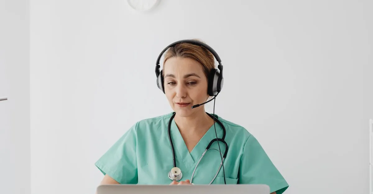 A doctor in scrubs using a laptop during a virtual consultation in a medical office.