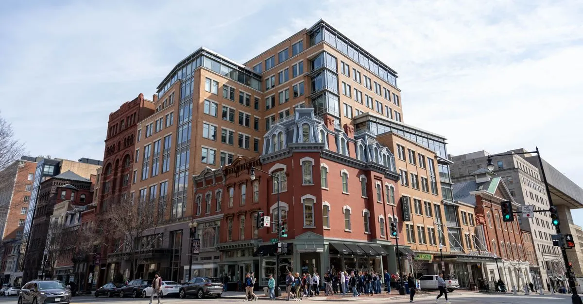 A downtown Washington, D.C. street corner with historic rowhouses and modern office buildings and pedestrians crossing.