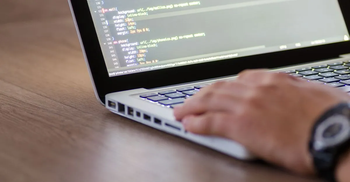 A developer at a laptop with CSS code on the screen, mid-build on a website.