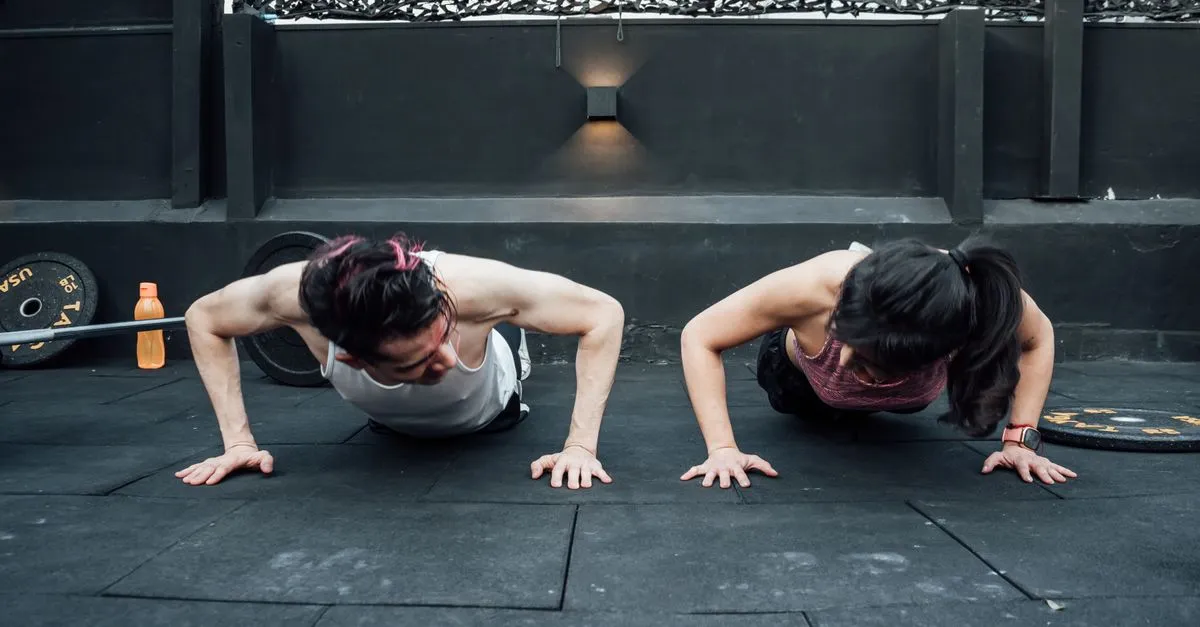 A man and a woman doing push-ups on the floor of an indoor gym, the kind of moment a gym website puts in its photo tour.