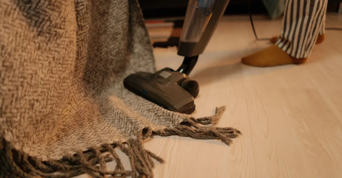 A carpet cleaner running a machine along the fringed edge of an area rug on a service call.