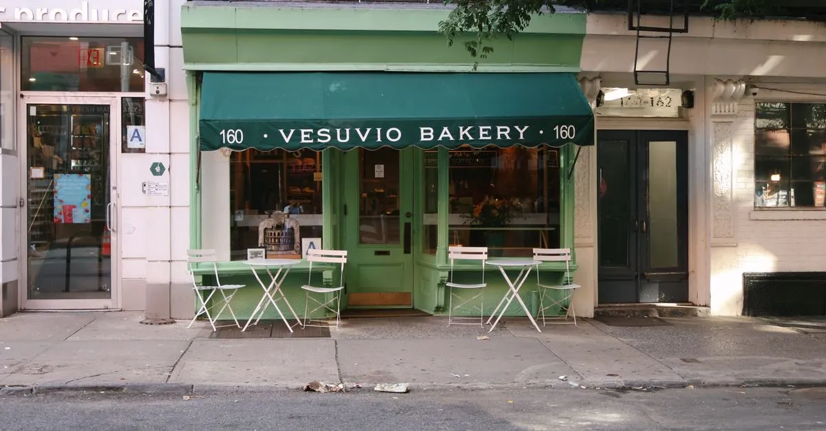 A New York City corner storefront bakery with a green awning on a busy street.