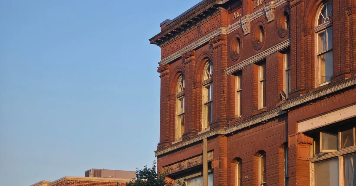 A historic red brick building facade with arched windows, dated 1894, glowing in warm sunset light against a clear sky.