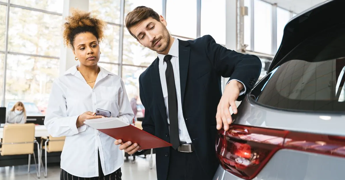 A dealership salesperson in a suit showing a customer the back of an SUV in the showroom, the kind of visit local search sends to the lot.