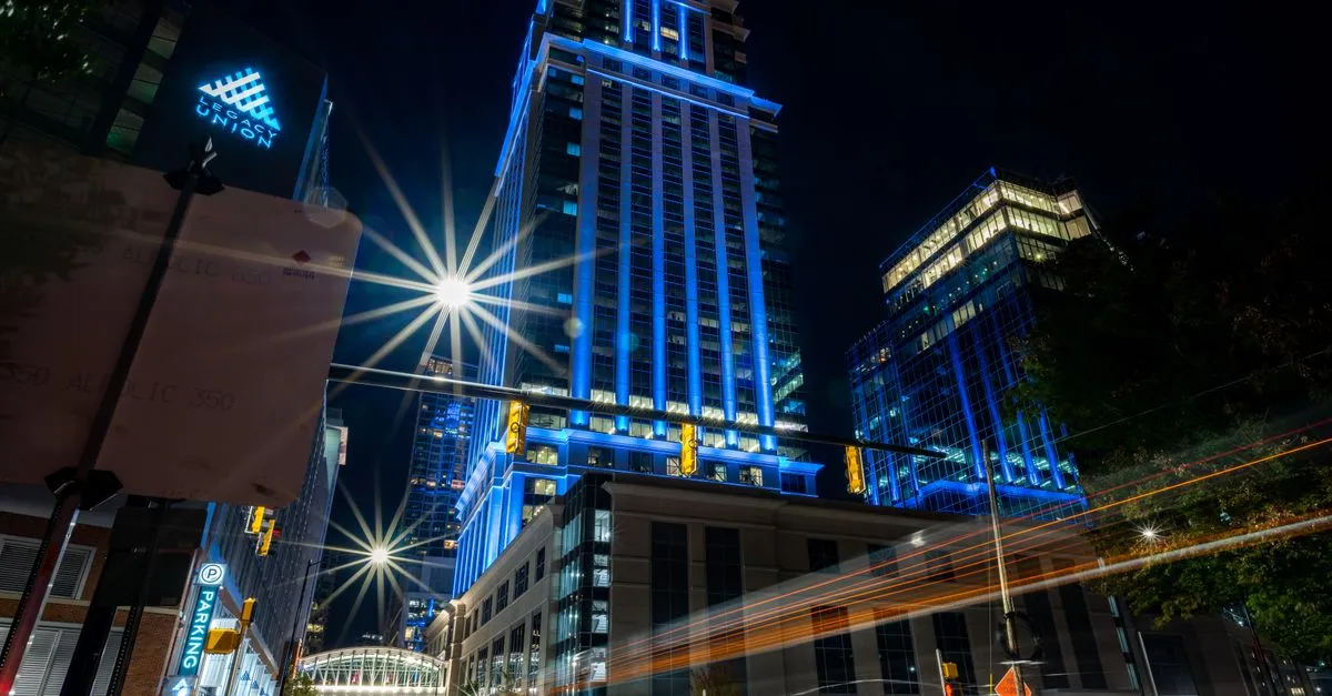 The Legacy Union bank towers lit blue at night over an Uptown Charlotte street, the numbered-Ward core of a banking metro where local search is decided.