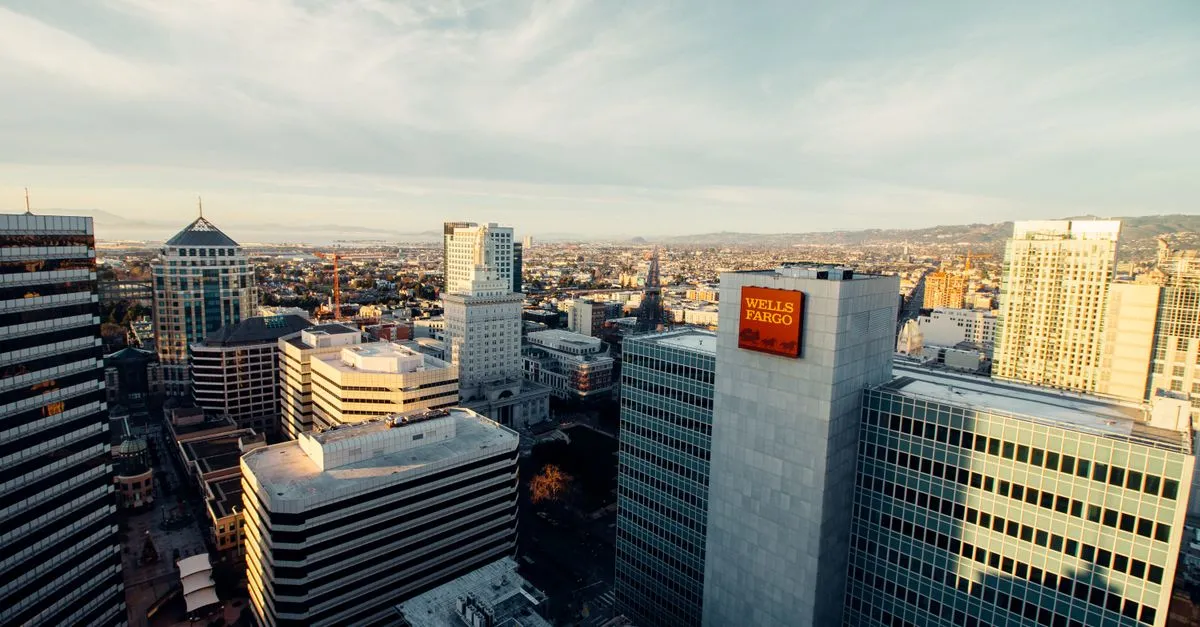 An aerial view of downtown Oakland, California at dusk, with the Tribune Tower spire and clustered office towers including one marked Wells Fargo.