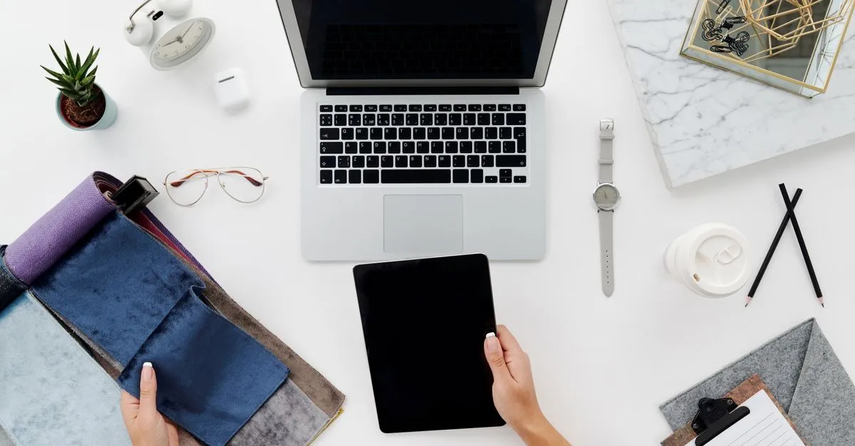 A designer workspace seen from above, with a laptop, a tablet, glasses, and a notebook laid out for a website build.