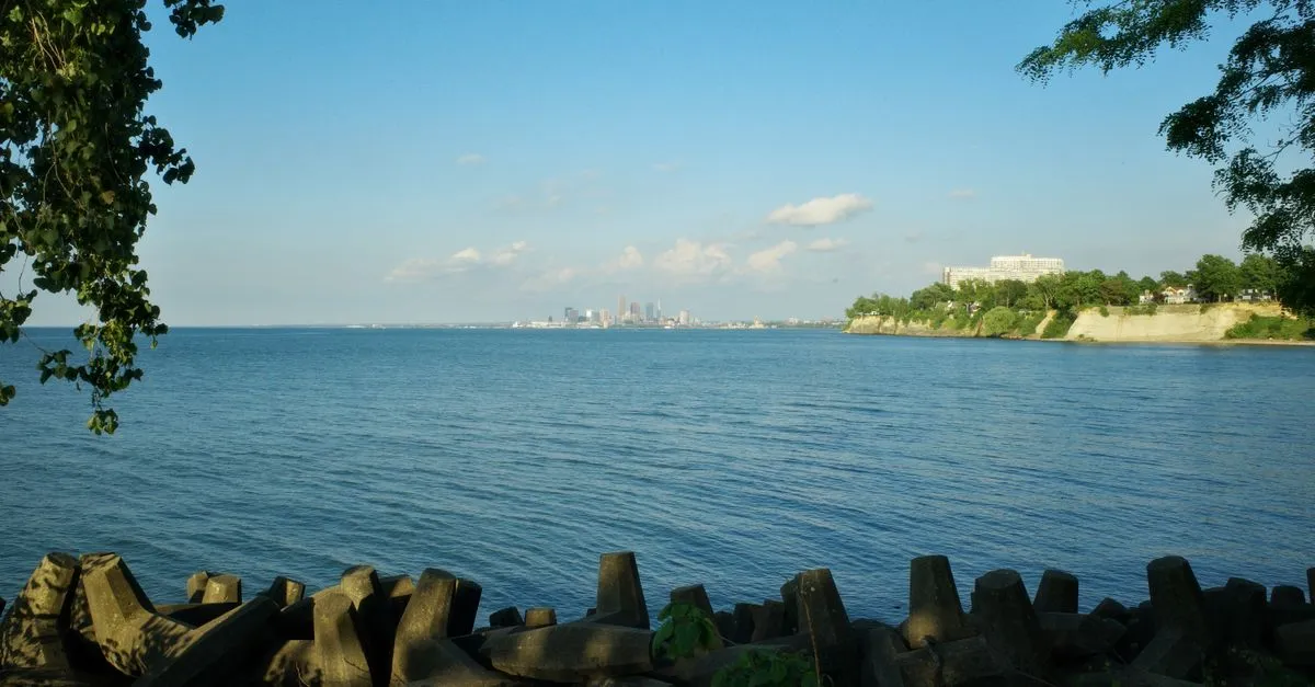 The Cleveland skyline in the distance across Lake Erie, seen from a tree-lined lakefront park in summer.