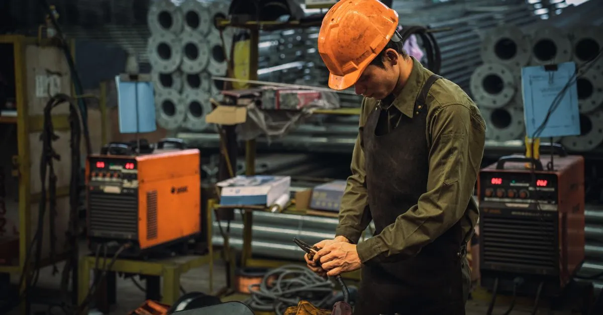 An engineer in safety gear operating a machine on a manufacturing plant floor.