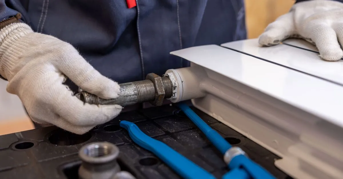 A plumber installing a radiator pipe with specialized tools on a service call.