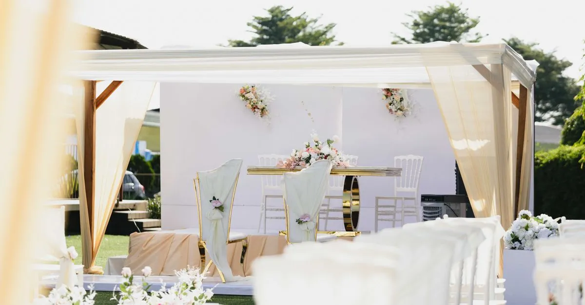 An outdoor wedding ceremony setup with white chairs and a floral arch, the setting couples search for when choosing a venue.