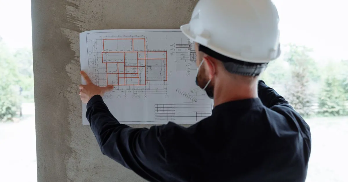 A contractor in a hard hat reviewing blueprints on a wall at a job site, the kind of general contractor buyers vet before they call.