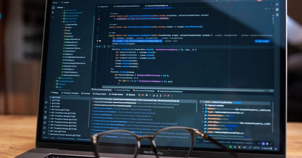 A laptop on a wooden desk showing lines of code in a dark editor, with a pair of glasses resting in front of the screen.
