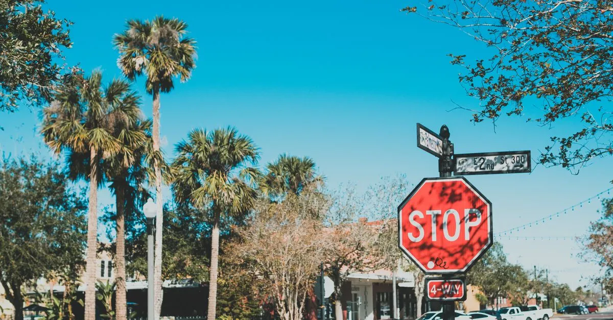 A palm-lined town street corner with a four-way stop sign and small storefronts under a clear blue sky, the kind of local business district a Jacksonville company competes in.