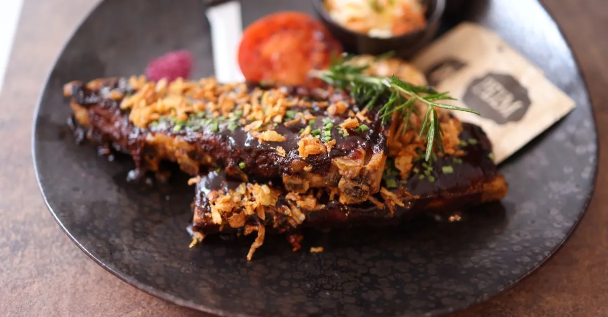 A plate of saucy barbecue ribs topped with crispy onions and fresh herbs, the kind of Kansas City plate people find with a near me search.