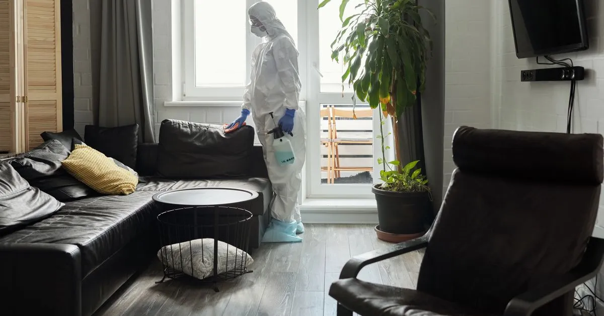 A pest control technician in protective gear spraying treatment inside a living room, the kind of home service that wins near me searches.