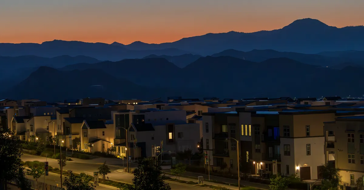 A modern master-planned neighborhood at dusk with desert mountains rising in the background.
