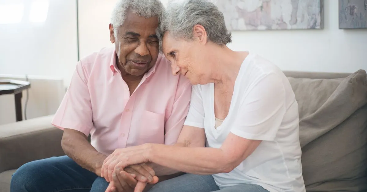 A home care caregiver sitting and talking with a senior client at home during a companion-care visit.