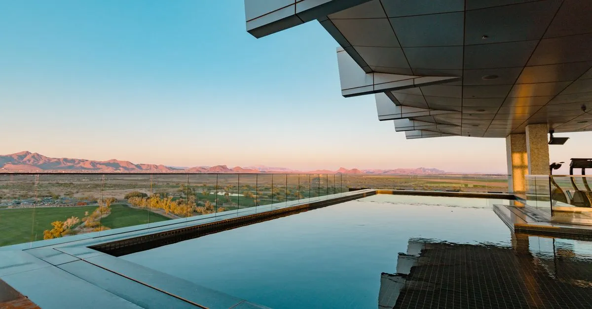 A luxury rooftop infinity pool overlooking the Sonoran desert mountains and a golf course at sunset in Arizona.