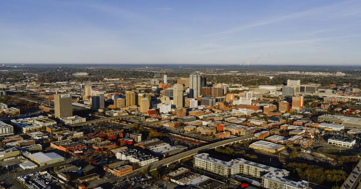 A daytime aerial view of downtown Birmingham, Alabama showing the UAB tower, brick buildings, and the surrounding cityscape.