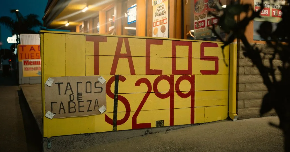 A bilingual taco stand storefront lit at dusk, its hand-painted signs advertising tacos and tacos de cabeza, the kind of neighborhood business the San Antonio map pack decides.