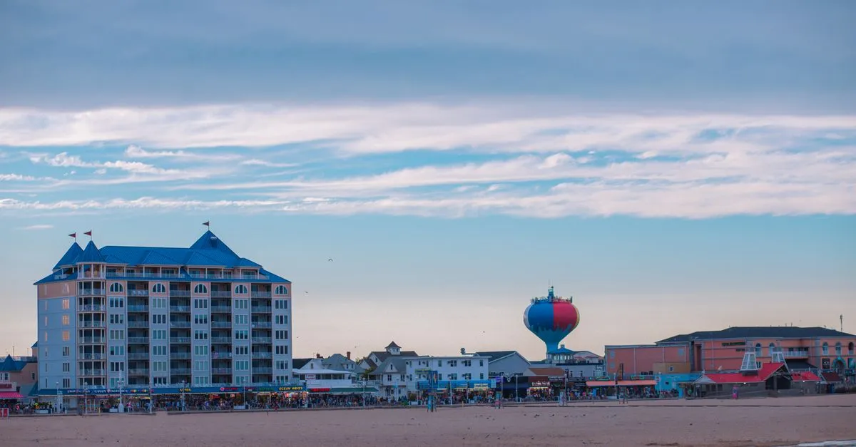 A resort beachfront lined with hotels and shops beside a wide sandy beach under a bright blue sky.