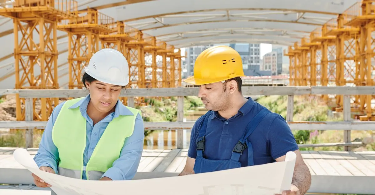 A project team in safety gear reviewing a blueprint on a jobsite, the kind of work a construction company website puts in its portfolio.