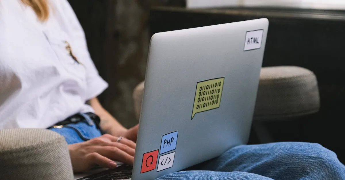 A person typing on a laptop covered in HTML, PHP, and code stickers, working on a website build.