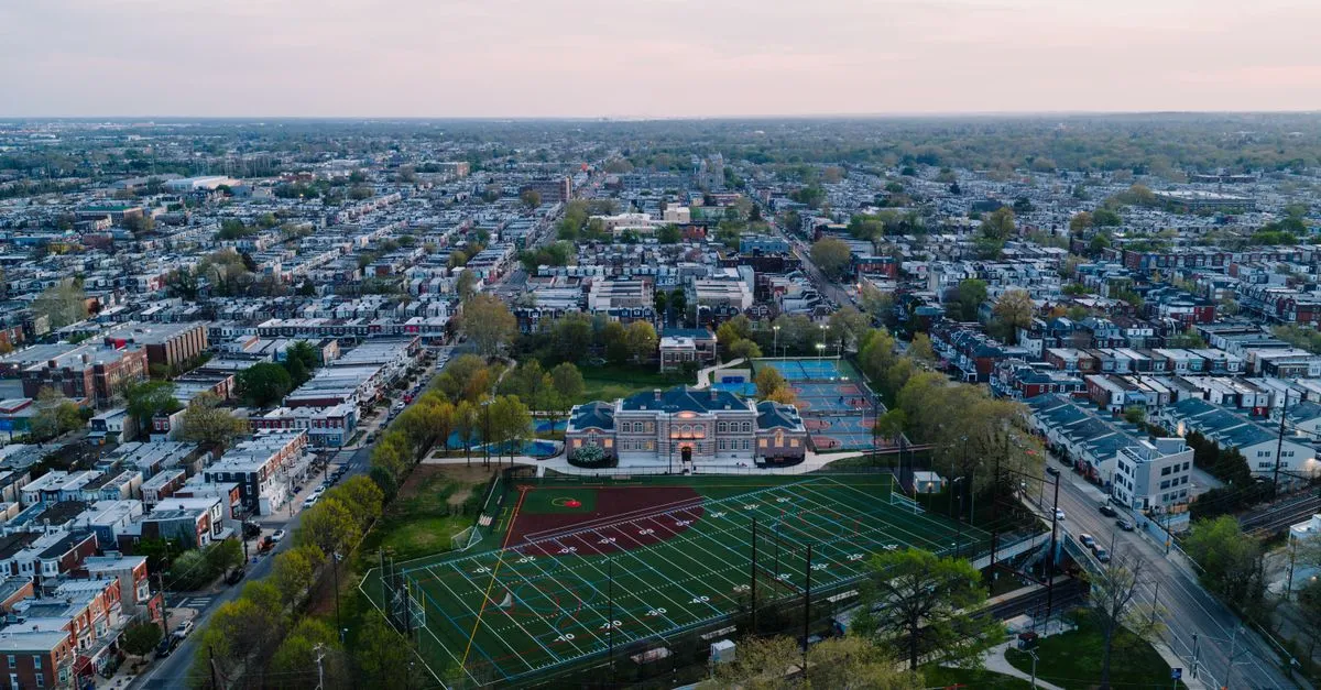 An aerial view of a dense Philadelphia rowhouse neighborhood laid out on the grid, block after block of homes around a school and playing field.