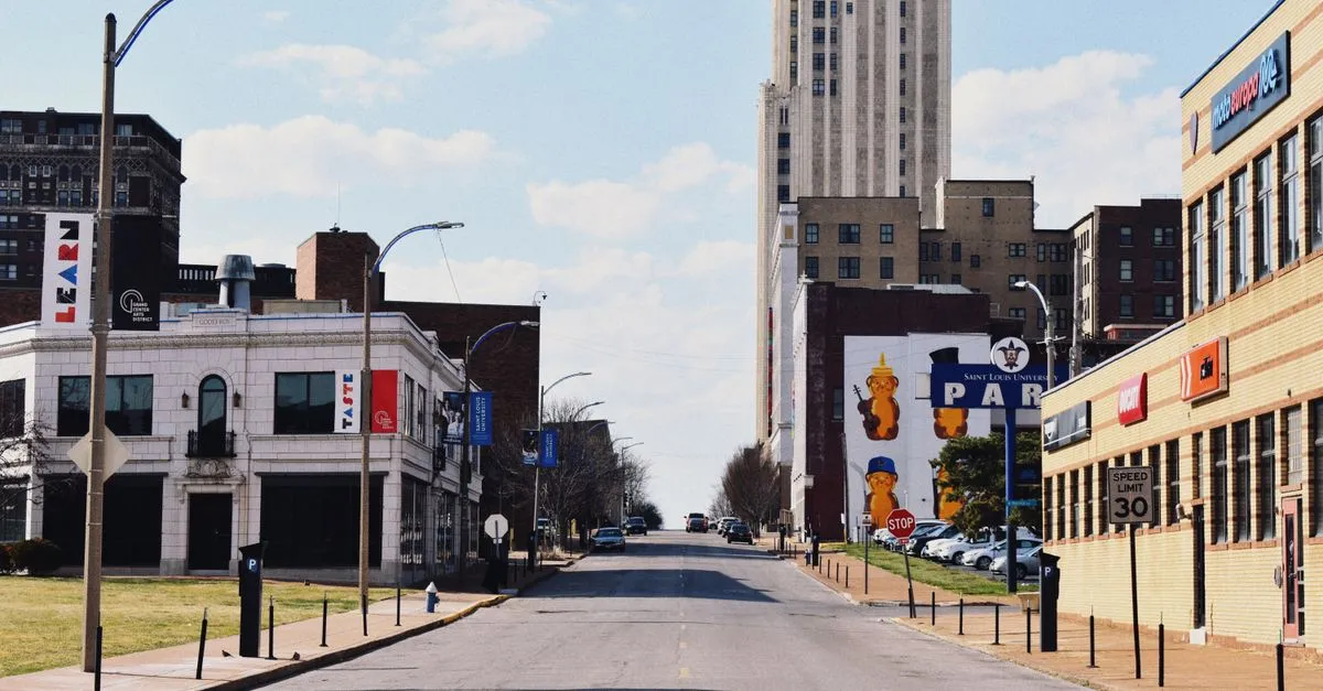 A downtown St. Louis street lined with historic brick buildings, with Saint Louis University signage and a mid-century tower rising in the distance.