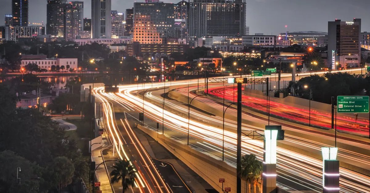 Long-exposure traffic light trails along the Interstate 4 corridor beneath the downtown Orlando skyline at dusk.