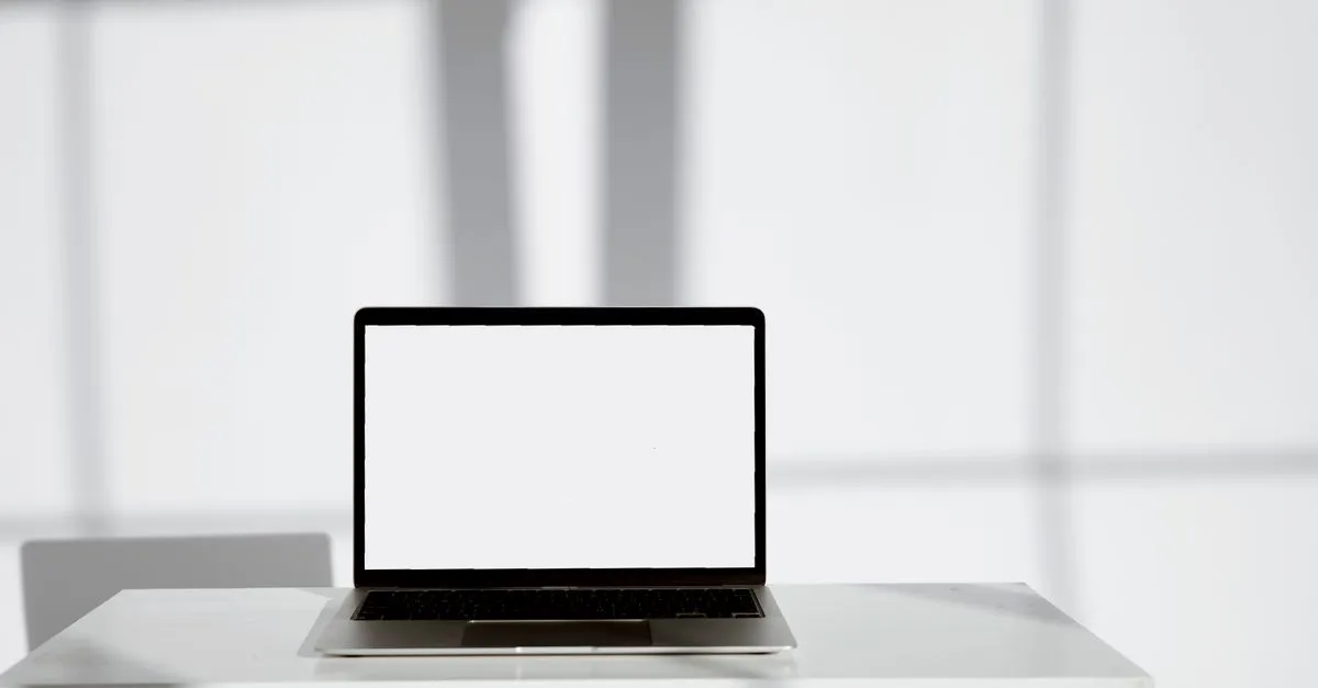 A laptop with a blank white screen on a clean white desk in a bright, sunlit room, ready for a website mockup.