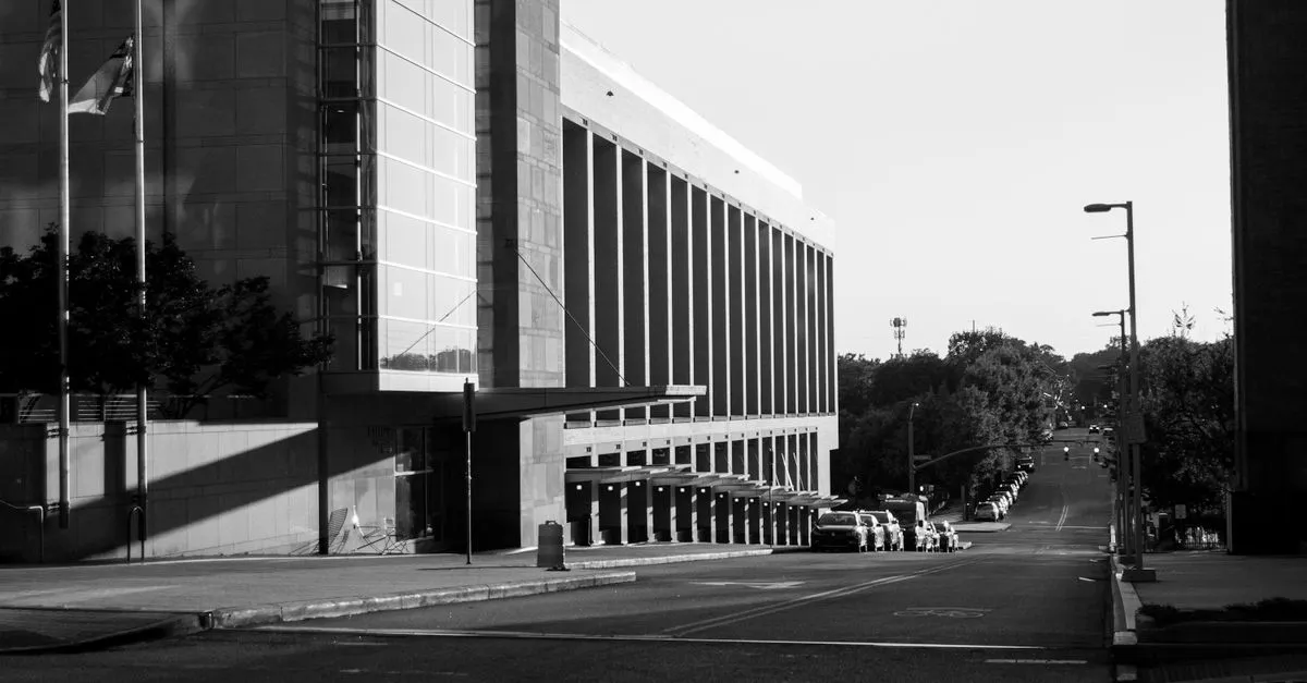 A black and white photo of a modern building with tall vertical columns on a quiet downtown street.