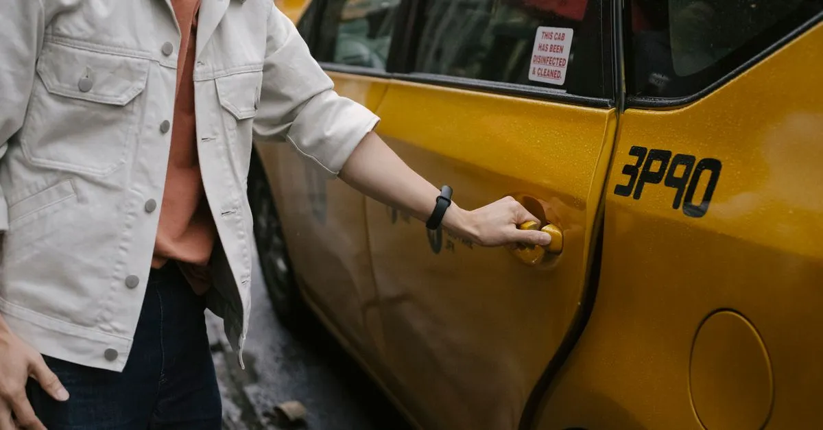A passenger opening the door of a yellow taxi cab parked at the curb on a city street.