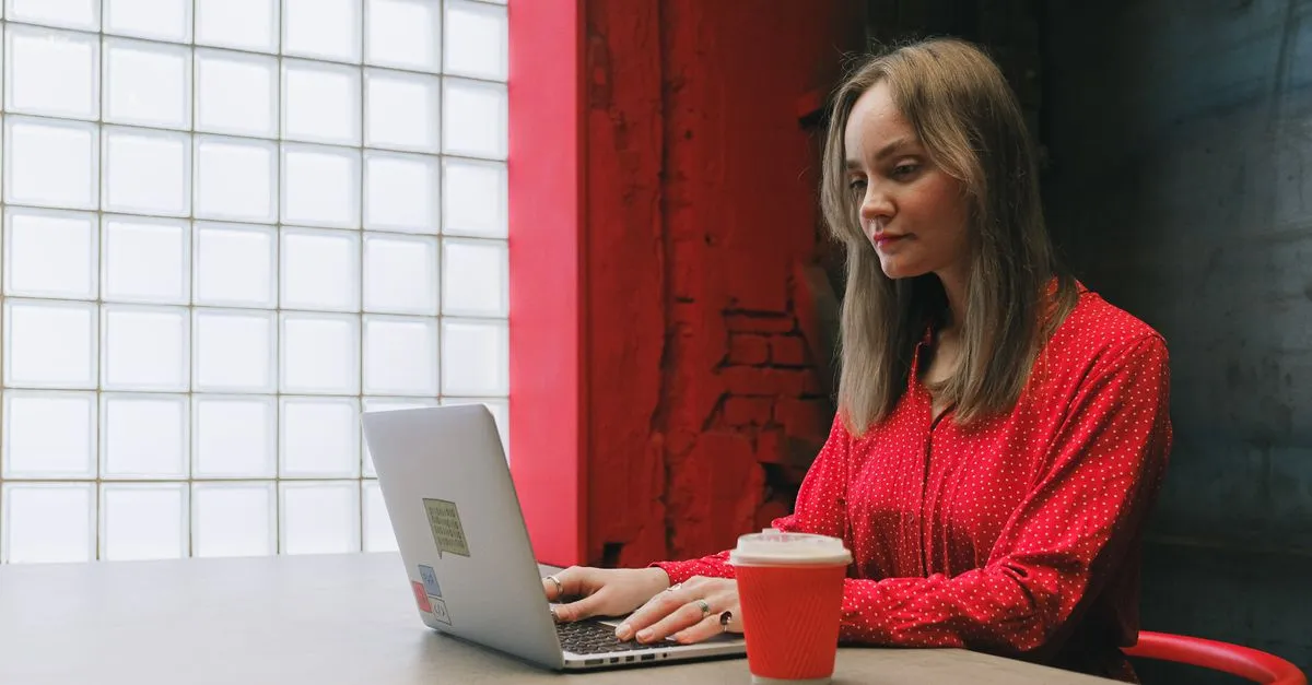 A web designer working on a laptop at a desk, a coffee beside her, focused on a website build.