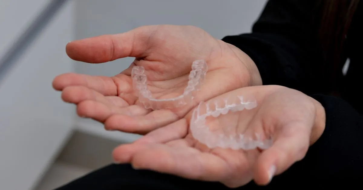 A patient holding two clear aligner trays, the Invisalign-style treatment an orthodontist offers alongside traditional braces.