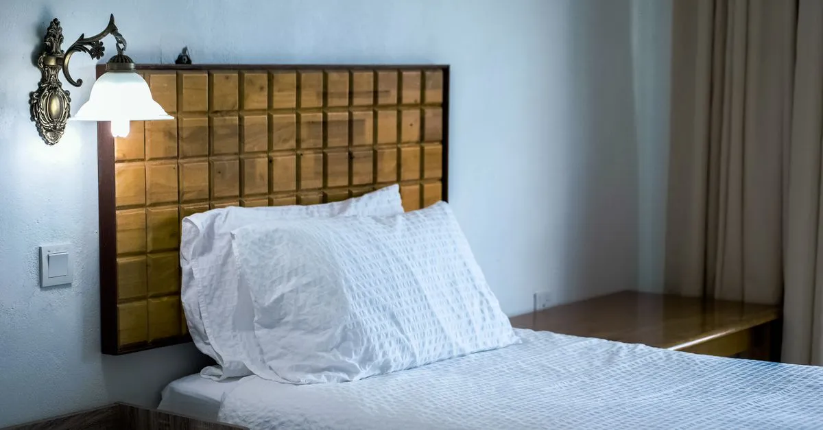 A styled hotel guest room with a wooden headboard, wall lamp, and crisp white bedding, the kind of room a hotel SEO page helps travelers book direct.