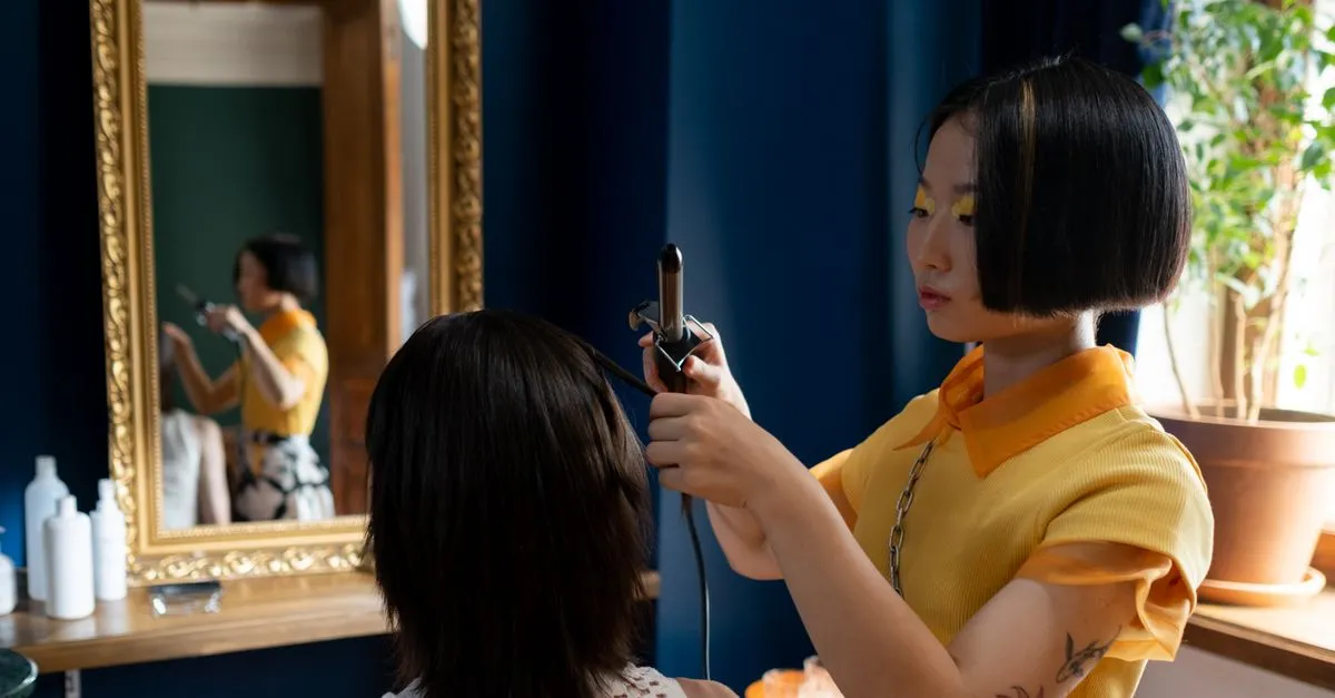 A hair stylist styling a client at a salon station with a curling iron, focused on the finished look.