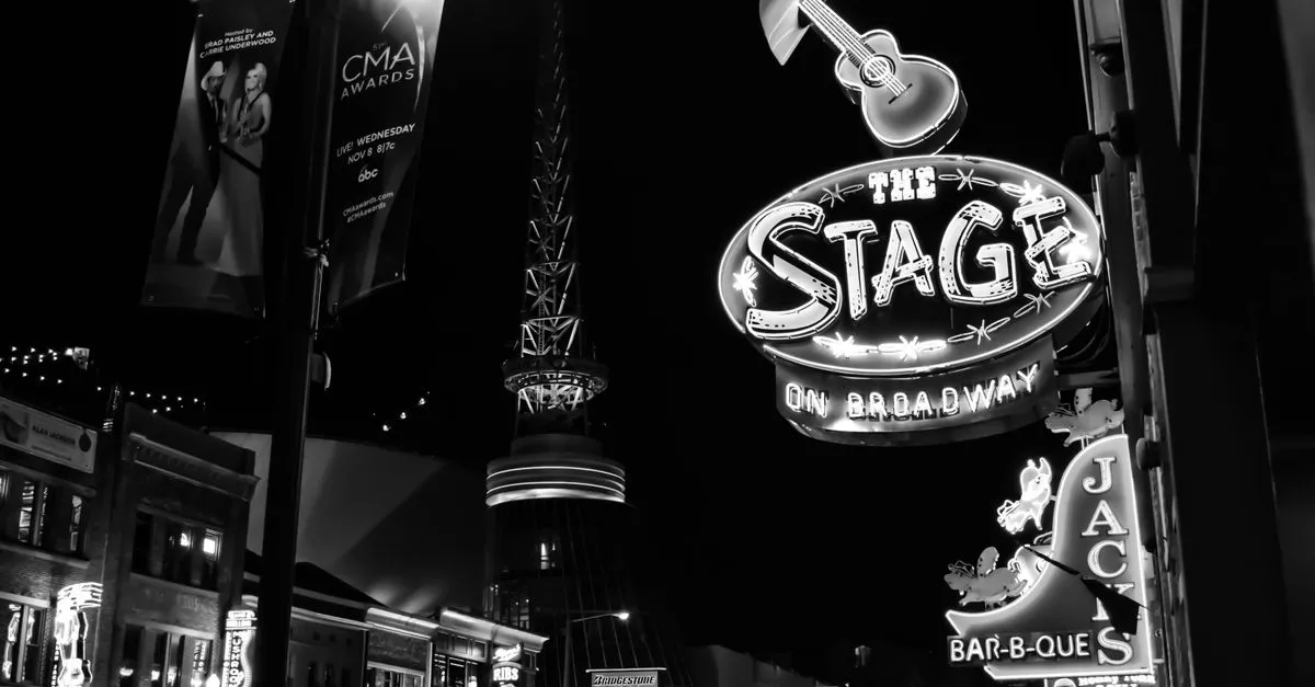 Neon signs of honky-tonk bars and music venues glowing along Broadway in downtown Nashville at night.
