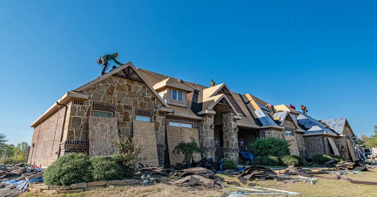 A roofing crew replacing the roof on a brick house on a clear day.