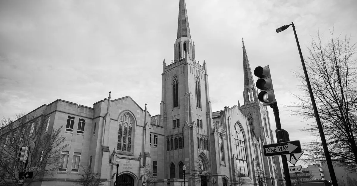 A historic Gothic-style stone church with tall spires on a downtown street corner in Tulsa, Oklahoma, under an overcast sky.