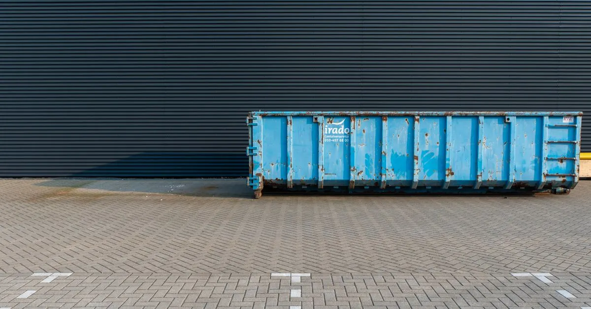 A blue roll-off dumpster staged in a paved service yard between hauls.